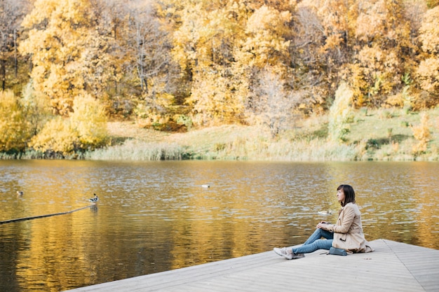 Mujer joven dibujando cerca de un lago en el bosque de otoño