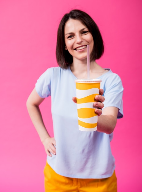 Mujer joven con dientes sensibles bebiendo agua fría sobre fondo de color