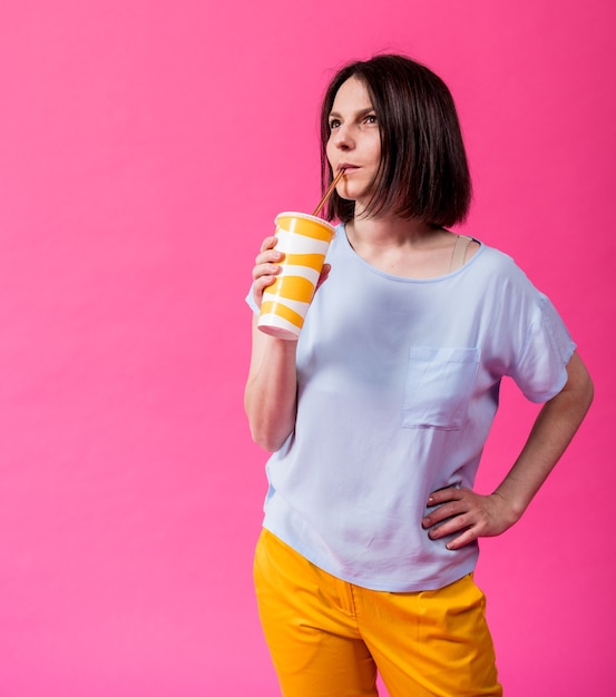 Mujer joven con dientes sensibles bebiendo agua fría sobre fondo de color