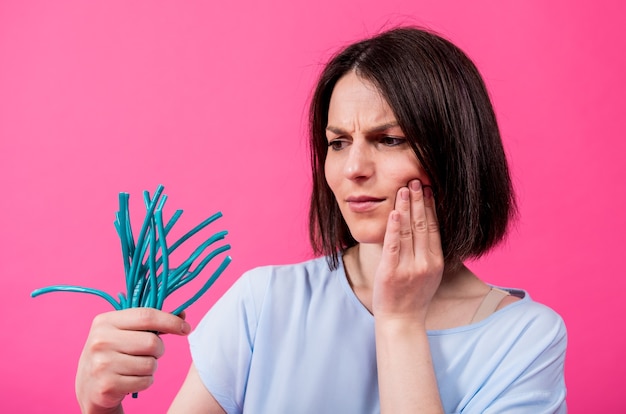 Mujer joven con dientes sensibles comiendo caramelos sobre fondo de color