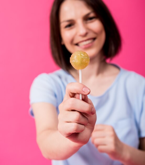 Mujer joven con dientes sensibles comiendo piruletas dulces sobre fondo de color