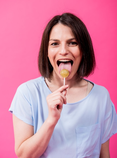 Mujer joven con dientes sensibles comiendo piruletas dulces sobre fondo de color