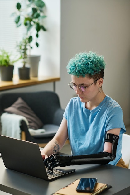 Mujer joven con discapacidad sentada en la mesa y trabajando en línea en la computadora portátil en la habitación