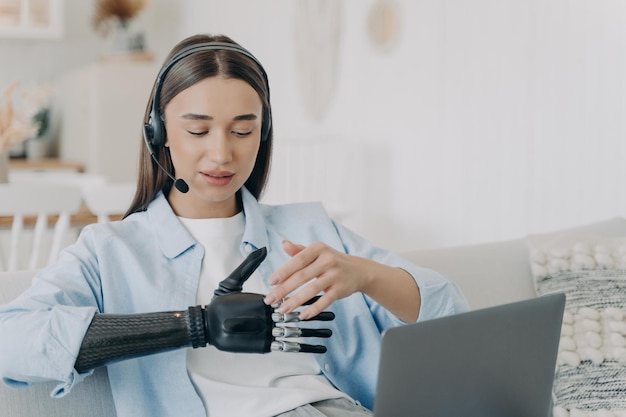 Mujer joven discapacitada con brazo artificial en auriculares en casa Freelancer tiene reunión en línea