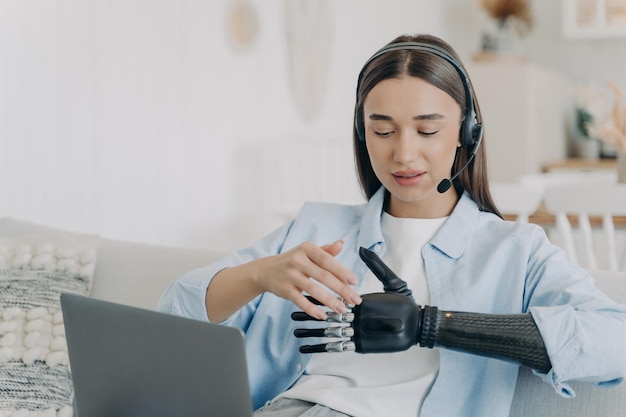 Mujer joven discapacitada con brazo artificial en auriculares en casa Freelancer tiene reunión en línea