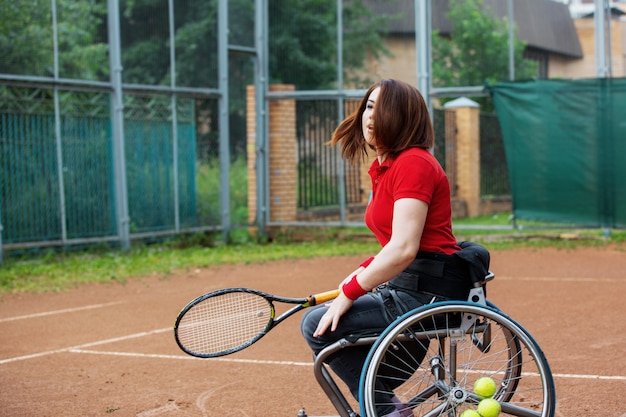 Mujer joven discapacitada en silla de ruedas jugando tenis en cancha de tenis