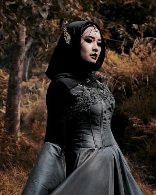 Mujer joven en disfraz de Halloween de pie en el bosque durante el otoño