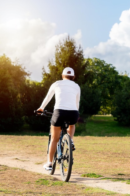 Mujer joven disfruta de un día soleado montando su bicicleta en el parque de la ciudad