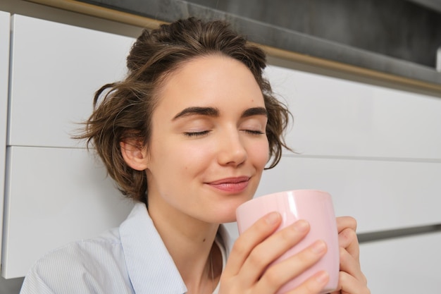 La mujer joven disfruta de su taza de café matinal, bebe té fresco y sonríe.