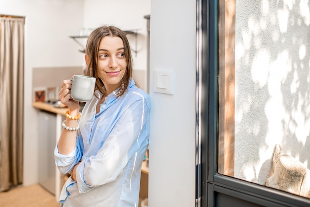 Foto mujer joven disfrutando de un café de pie en la pequeña cocina de la casa de campo