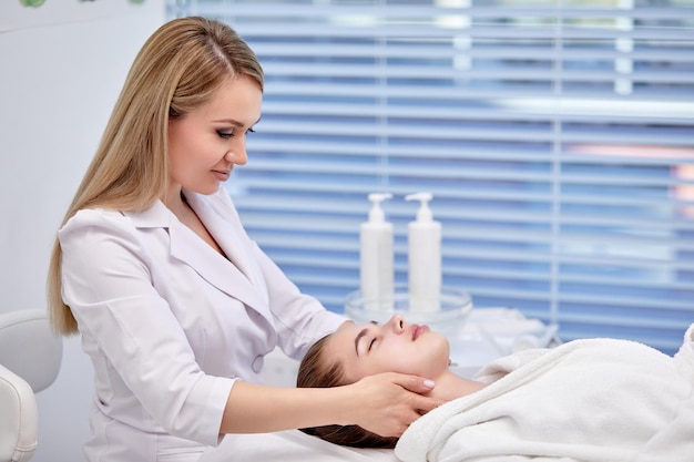 Mujer joven disfrutando de masaje facial anti envejecimiento señora bonita recibiendo cuidado profesional de la piel en wellnes ...