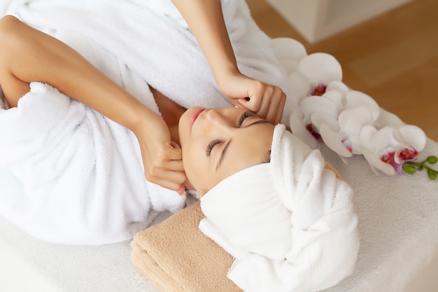 Mujer joven disfrutando de masaje facial en el salón de spa.