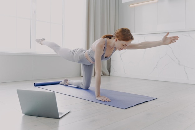 Mujer joven disfrutando del yoga con lecciones en video Ejercicio matutino y concepto de rutina deportiva