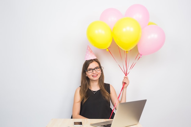 Mujer joven divertida celebrando el éxito de su negocio o un cumpleaños en la oficina sosteniendo coloridos globos de fiesta.