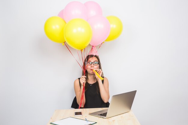 Mujer joven divertida celebrando el éxito de su negocio o un cumpleaños en la oficina sosteniendo coloridos globos de fiesta.