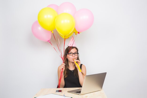 Mujer joven divertida celebrando el éxito de su negocio o un cumpleaños en la oficina sosteniendo coloridos globos de fiesta.