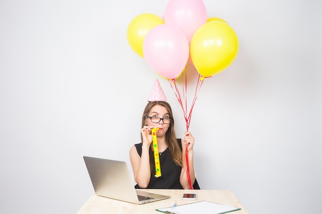 Mujer joven divertida celebrando el éxito de su negocio o un cumpleaños en la oficina sosteniendo coloridos globos de fiesta.