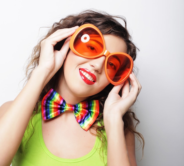 Mujer joven divertida con grandes gafas de sol naranjas sobre blanco