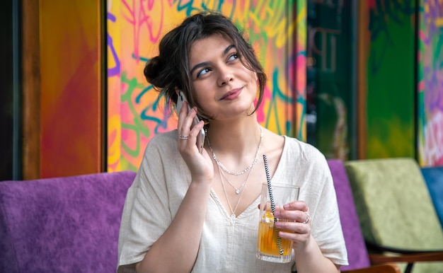 Mujer joven divertida hablando por teléfono con un vaso de limonada