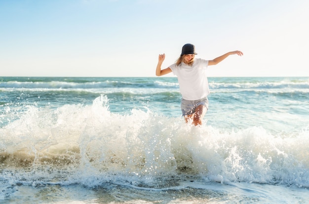 Mujer joven divertida juguetona en la playa al atardecer. Hermosa mujer feliz en la orilla del mar azul divirtiéndose jugando salpicaduras de agua, estado de ánimo positivo, vacaciones de verano, concepto soleado