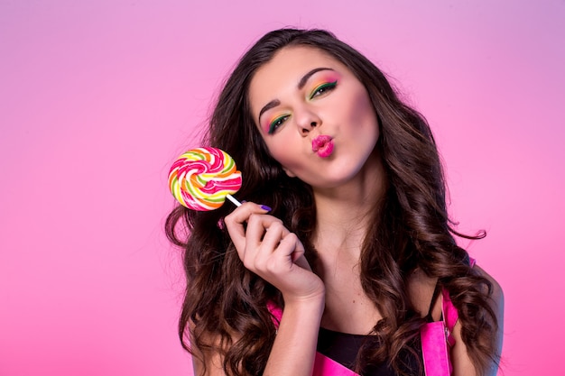 Mujer joven divertida en mono con piruleta y posando y besando