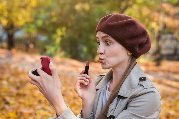 Mujer joven divertida que sostiene el lápiz labial en sus manos y hace selfie.