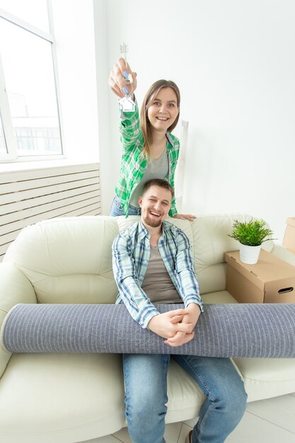 Mujer joven divertida y su marido sosteniendo en las manos las llaves de su nuevo apartamento mientras está sentado