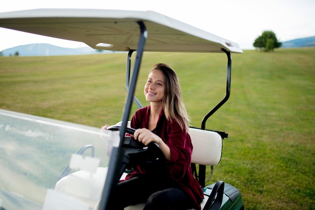 Mujer joven diviértete con el coche de golf buggy en un campo en las montañas