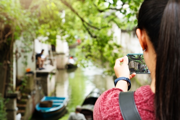 Mujer joven divirtiéndose en la ciudad del canal local en China con la cámara en el teléfono inteligente haciendo fotos