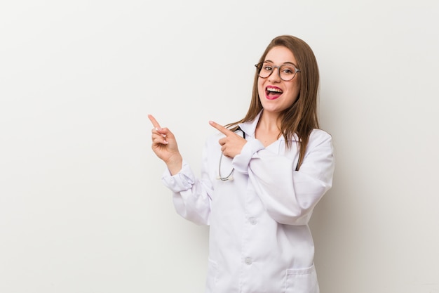 La mujer joven del doctor contra una pared blanca excitó sostener un espacio de la copia en la palma.