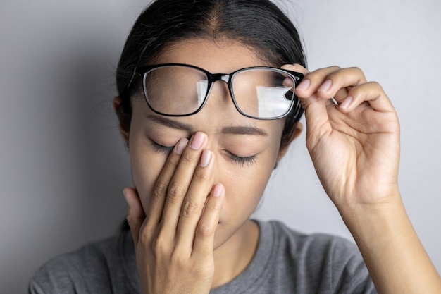 Mujer joven con dolor de ojos en un gris.