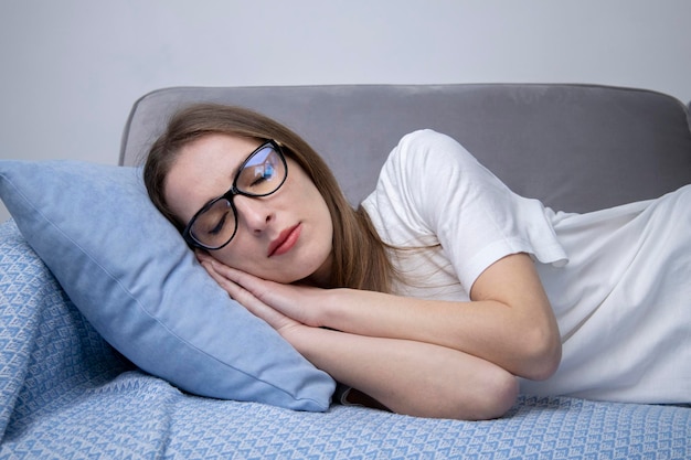 Foto mujer joven dormida en una camiseta blanca con gafas en un sofá