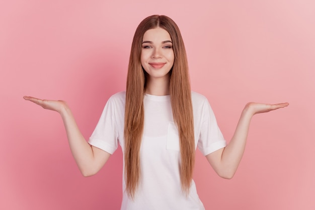 Mujer joven dos manos sosteniendo copyspace productos publicitarios imaginarios en pared rosa