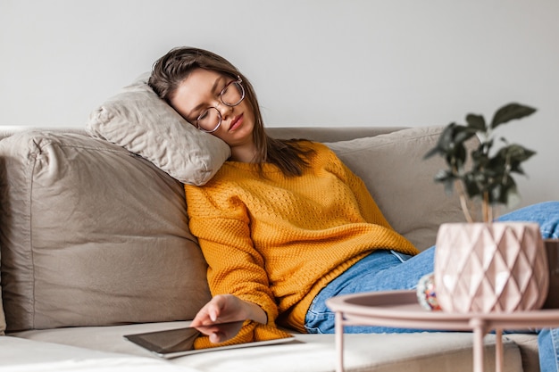 Mujer joven duerme en el sofá con tableta digital