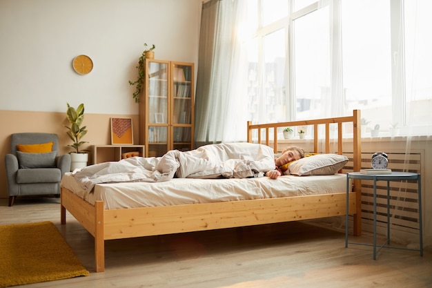 Mujer joven durmiendo en la cama por la mañana en el dormitorio moderno