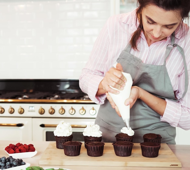 Foto mujer joven, elaboración, cima cremosa, de, cupcakes, primer plano