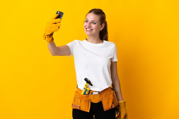 Mujer joven electricista aislada en amarillo haciendo un selfie