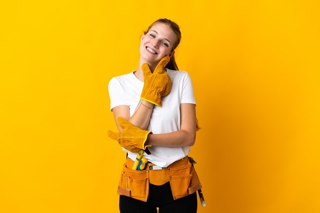 Mujer joven electricista aislada en amarillo sonriendo