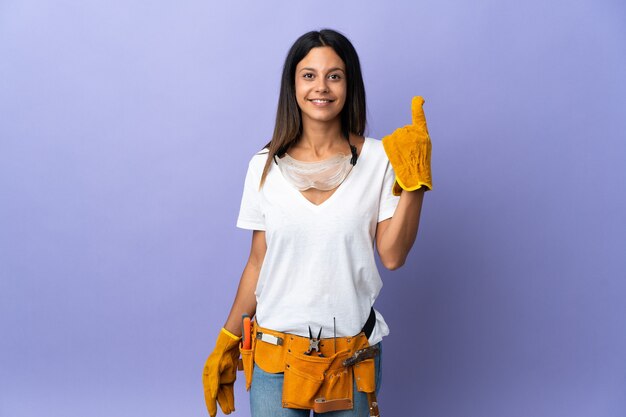 Mujer joven electricista aislada en la pared púrpura apuntando hacia una gran idea