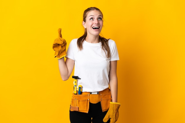 Mujer joven electricista en amarillo apuntando hacia arriba y sorprendido