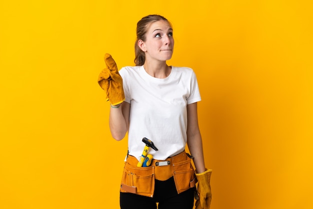 Mujer joven electricista en amarillo con los dedos cruzando y deseando lo mejor