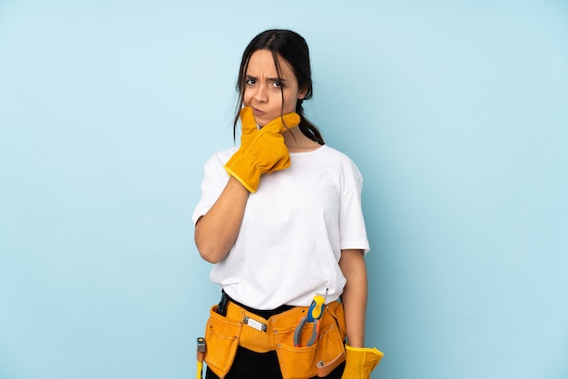 Mujer joven electricista en pensamiento de pared azul