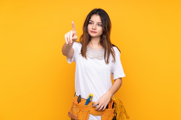 Mujer joven electricista sobre aislado en amarillo tocando en pantalla transparente