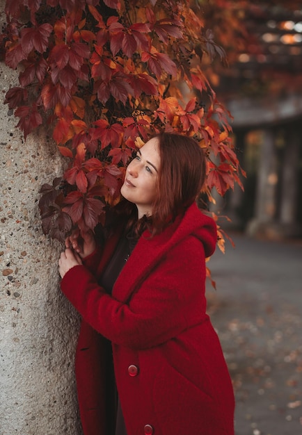 Mujer joven elegante en un abrigo casual burdeos en otoño Modelo lindo camina en el parque en otoño dorado a través de árboles coloridos y hojas caídas Paseo de otoño naturaleza colorida