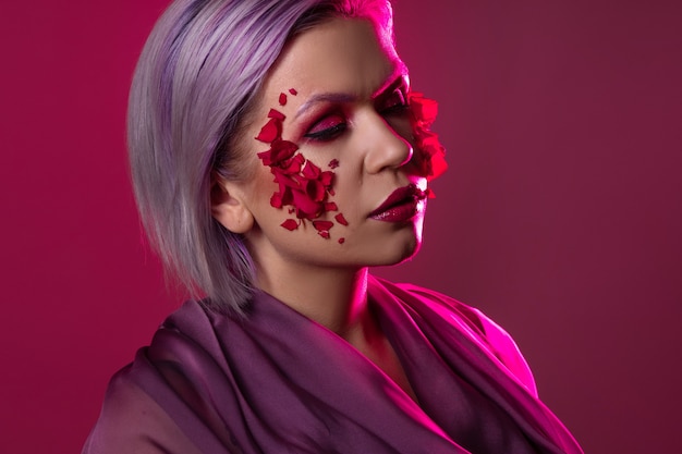 Mujer joven elegante y brillante con maquillaje de colores y pétalos de flores en el rostro