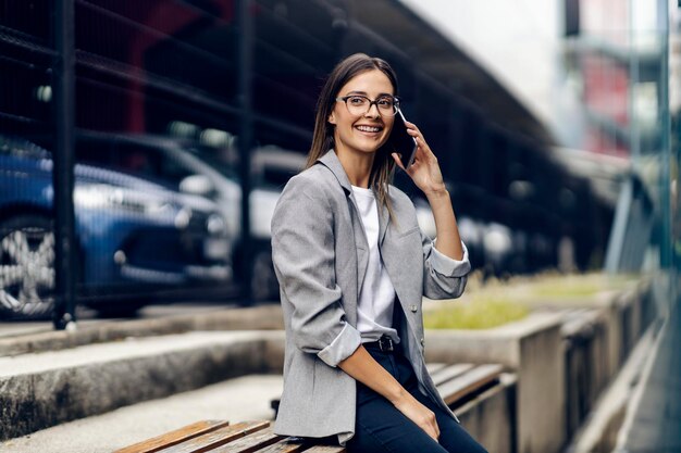 Una mujer joven y elegante feliz está sentada al aire libre y tiene una llamada telefónica