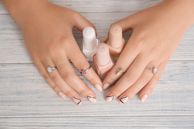 Mujer joven con elegante manicura y esmaltes de uñas en mesa de madera, vista superior