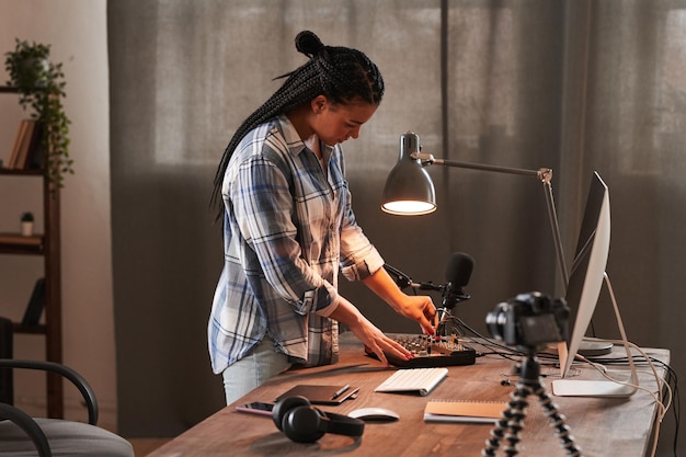 Mujer joven elegante de pie en la mesa en la sala de oficina en casa tipo loft y encendiendo el micrófono antes