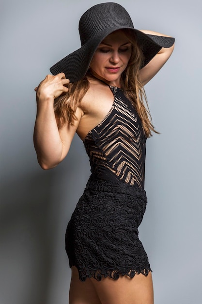 Mujer joven elegante en ropa de playa de moda y sombrero negro sobre un fondo gris Vertical