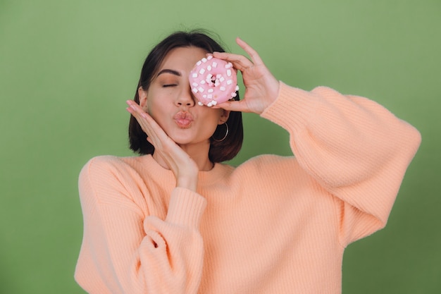 Mujer joven elegante en suéter de melocotón casual aislado en la pared verde oliva enviar beso con espacio de copia de rosquilla rosa